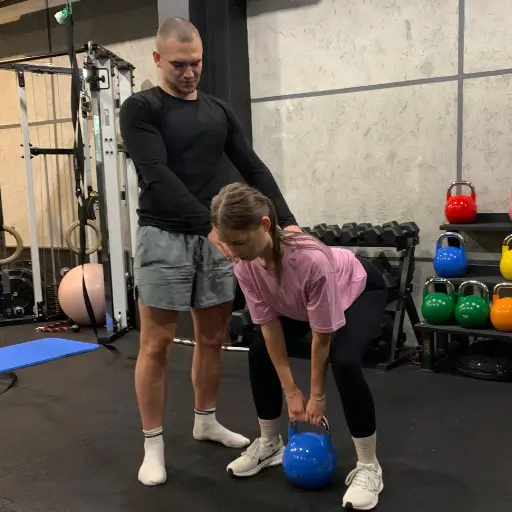 Marcel Gielezy uczy klientkę na siłowni ćwiczyć z kettlebells