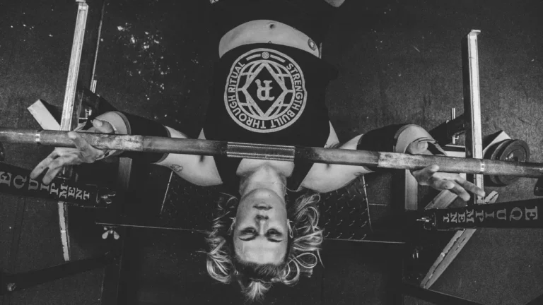 Zawodniczka trójboju siłowego leży na ławce do wyciskania i przygotowuje się do wyciskania sztangi leżąc