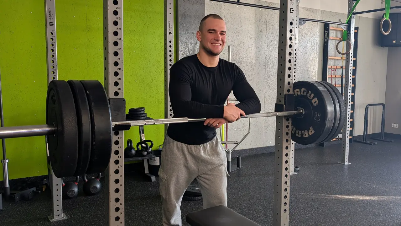 Trener personalny Marcel Gielezy stoi przy ławeczce treningowej na siłowni i przygotowuje się do serii wyciskania leżąc