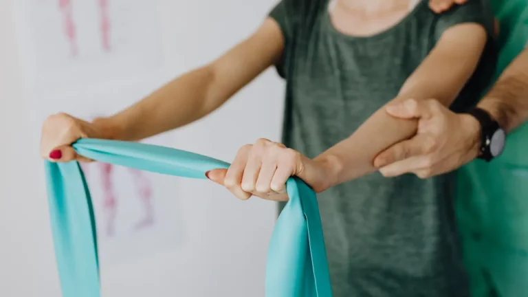 Pacjent wykonuje ćwiczenie prehabilitacyjne na staw ramienny z gumą oporową pod okiem trenera medycznego